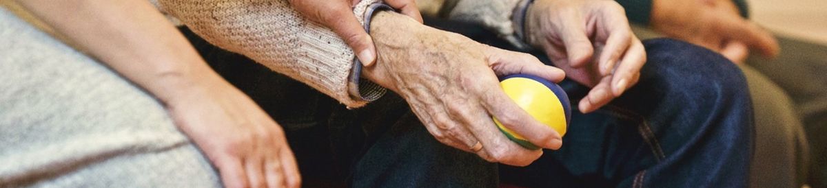 Ein Ausschnitt 3 ältere Personen sitzen nebeneinander auf einem Stuhl, und halten die Hände